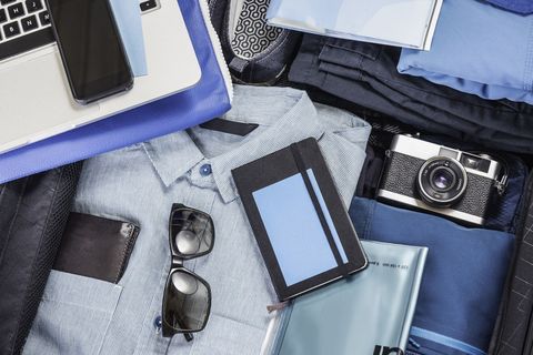 Overhead detail of packed suitcase with blue shirt, retro camera, laptop, smartphone and notebook