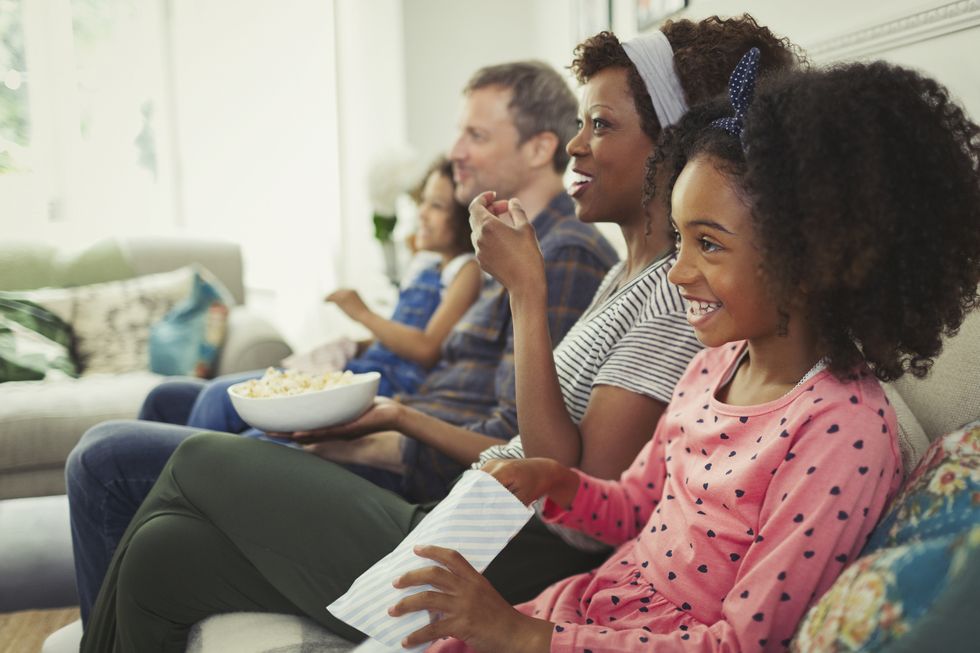 Young multi-ethnic family watching movie and eating popcorn on sofa