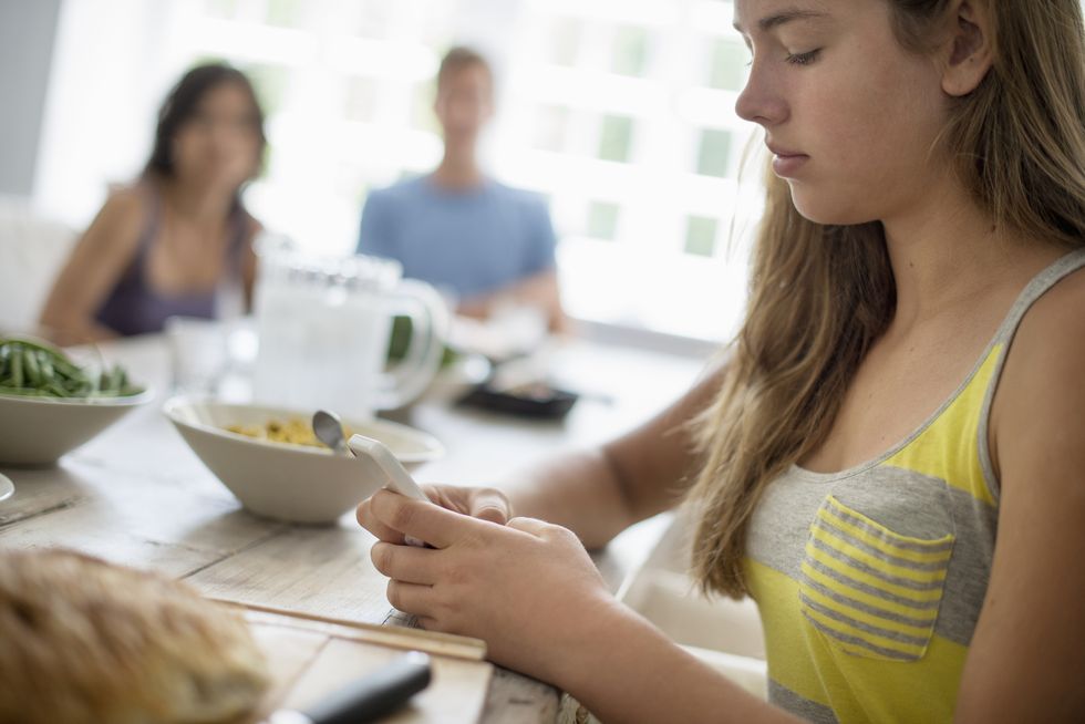 A young girl seated checking her smart phone at a dining table