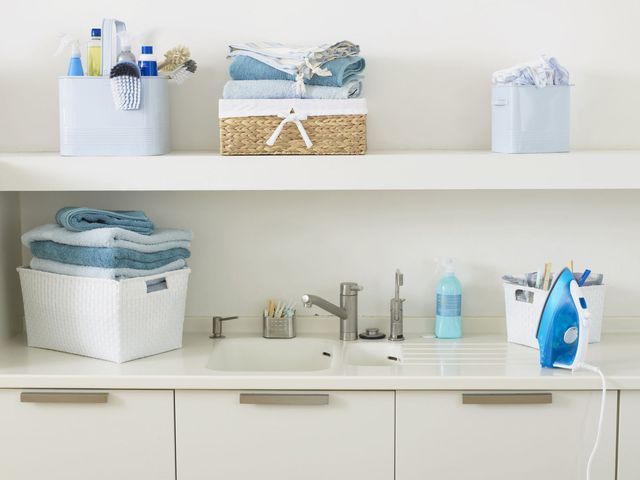 Items used for washing and cleaning, and stack of folded towels, next to and on shelf above sink in domestic laundry room