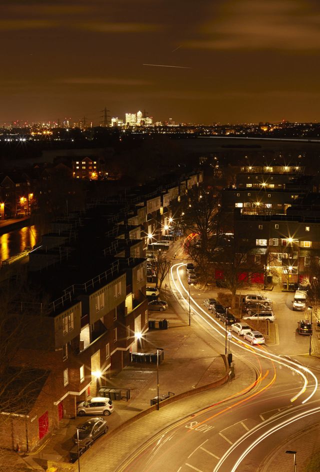 Low rise London housing in Tottenham Hale with Canary Wharf city skyline in the background. Light trails from cars.