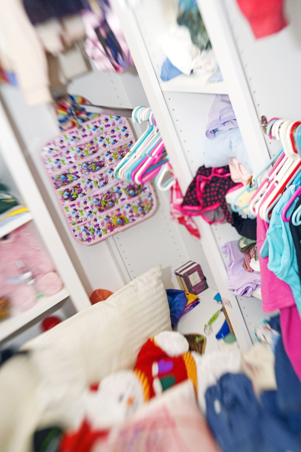 Messy white closet with children's clothing and toys
