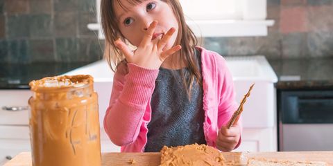 Girl making peanut butter sandwich, licking fingers