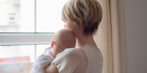 Mother holding baby looking out the window sad