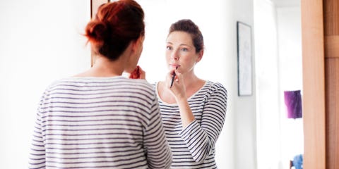 Woman applying makeup lipstick in the mirror