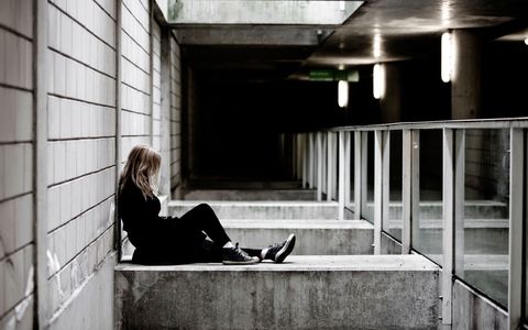 Young woman sits alone against a concrete pillar