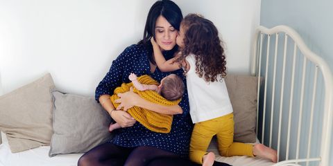 Mother holding newborn in her arms, big sister kissing her mother