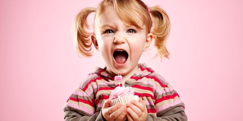 Cute litte girl dirty laughing and holding pink birthday cupcake