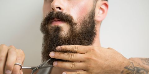 Man with tattoos and bushy beard cutting facial hair