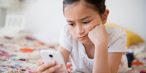 Sad young girl looking at her phone while lying on bed