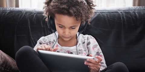 Girl sitting on sofa using digital tablet and headphones