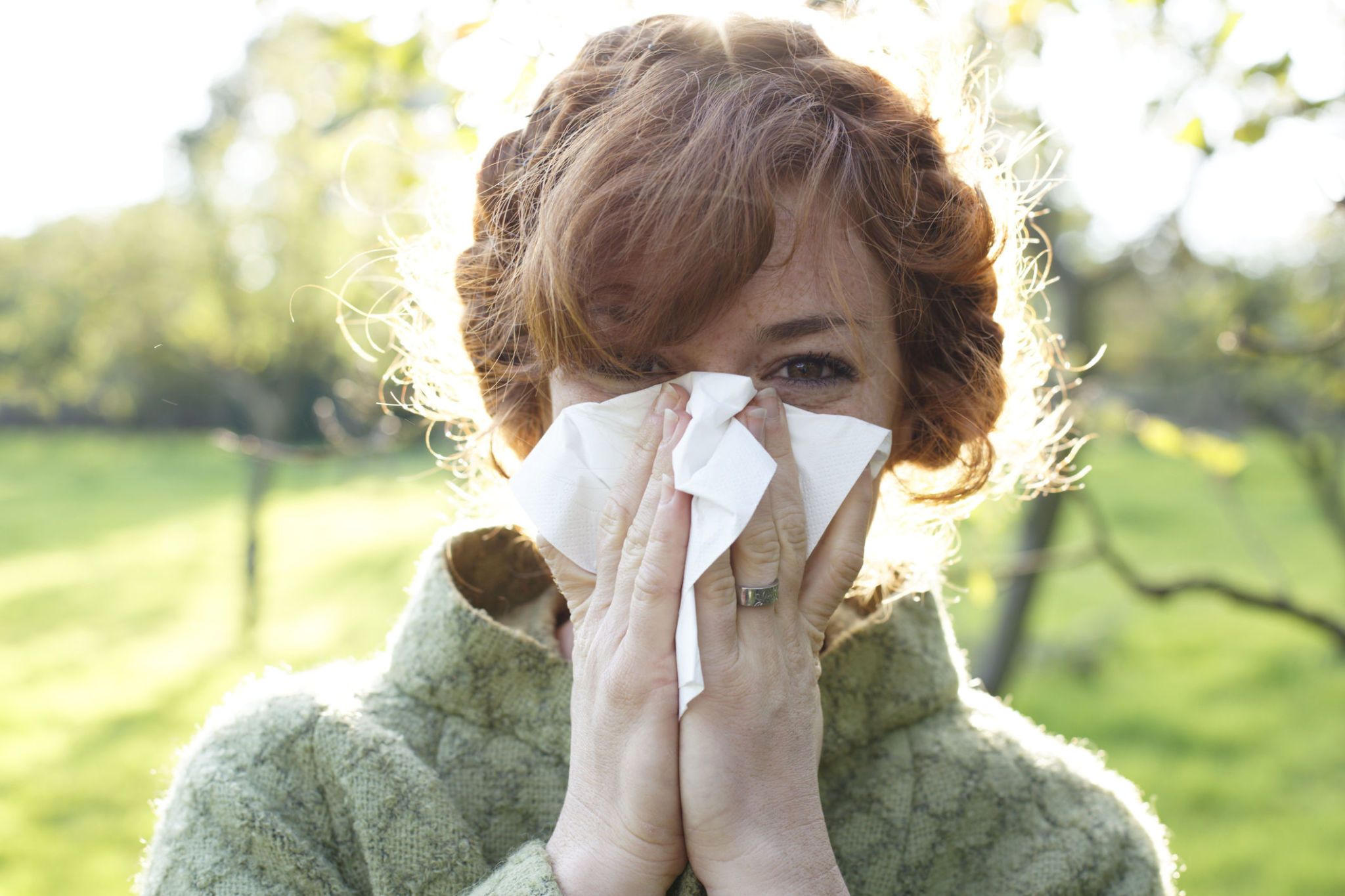 Woman sneezing and blowing her nose in a field