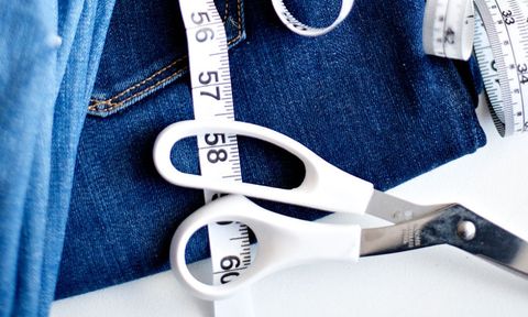 Pair of blue jeans with white scissors and measuring tape