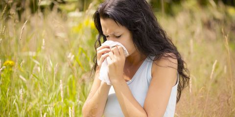 Woman with hay fever blowing her nose surrounded by pollen