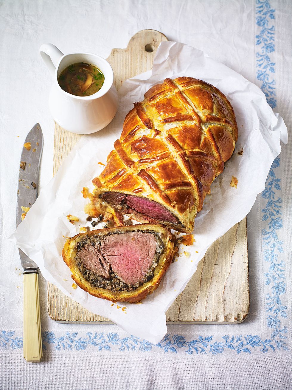 a medium rare beef wellington, sliced on a wooden board on a white and blue tablecloth
