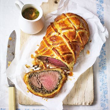 a medium rare beef wellington, sliced on a wooden board on a white and blue tablecloth