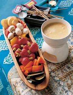 a pot of cheese fondue and a plate of vegetables and sticks