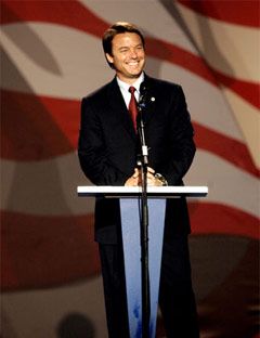 john edwards in front of podium and mic smiling