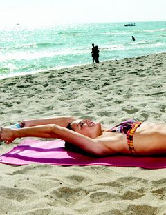 girl lying on beach with water bottle over her head