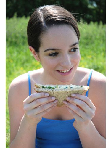 girl sitting in the grass eating a sandwich