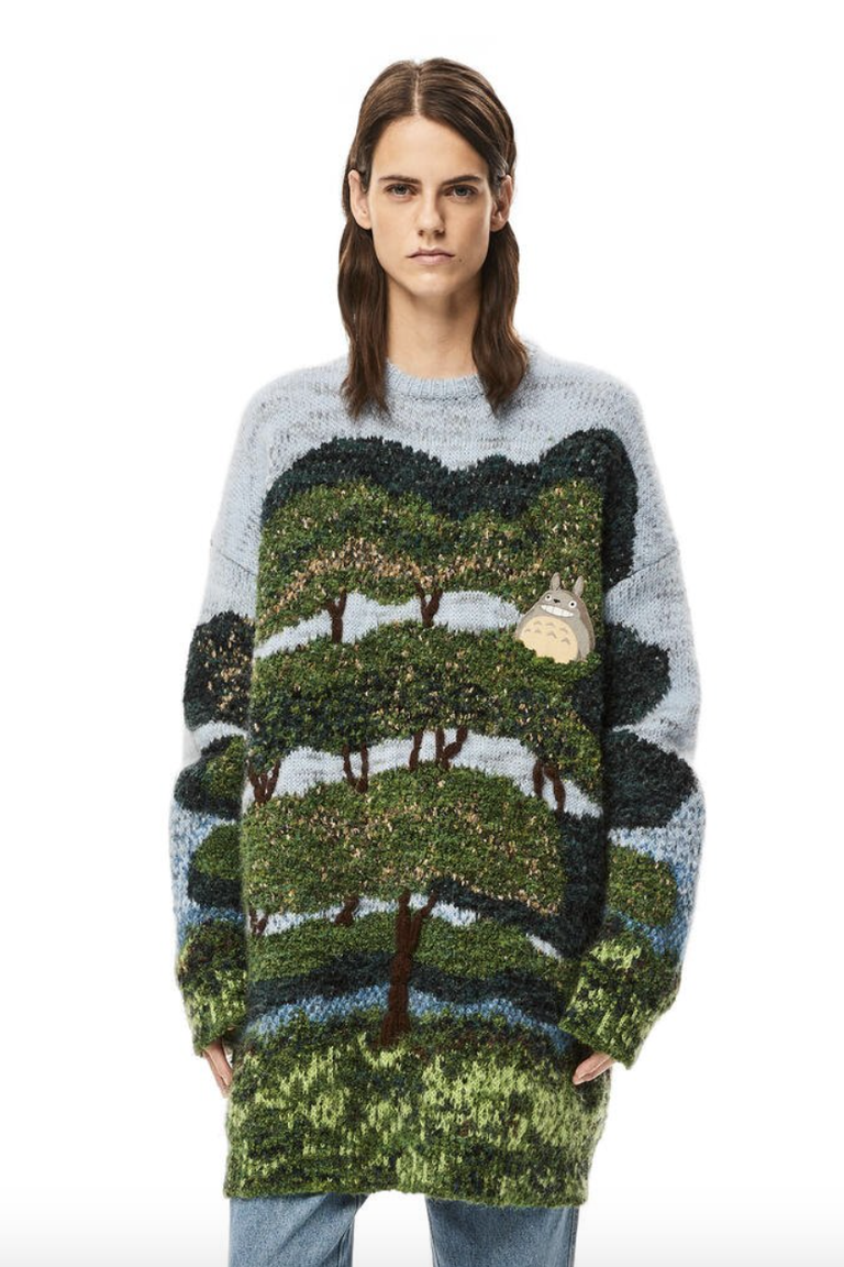 a model wearing a below the knee knitted jumper that consitis of a blue sky and a giant tree in various greens with a totoro patch on the left breast area
