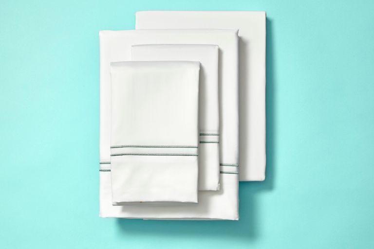 a white sheet set with hem detailing from the company store on a turquoise background, good housekeeping's choice for best wrinkle resistant cotton sheets