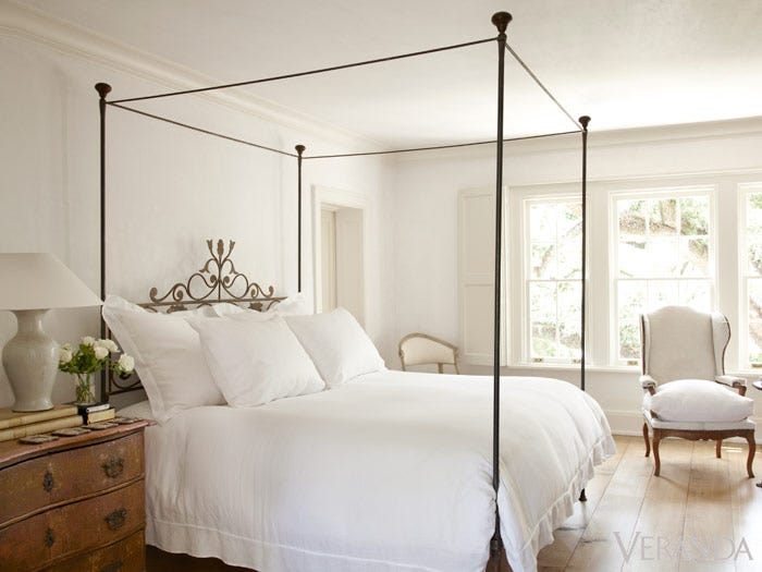 White bedroom decor in a French Country house by Pamela Pierce. Poster bed, antique chest, wing chair, and chestnut wood floors. #bedroomdecor #frenchcountry #whitebedroom #pamelapierce #posterbed