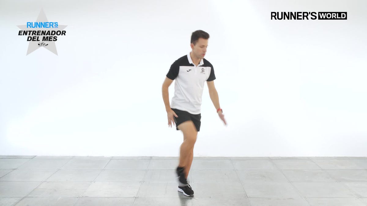 full length side view of caucasian man in red singlet, black shorts and shoes, striding along sidewalk during summertime weekend workout.