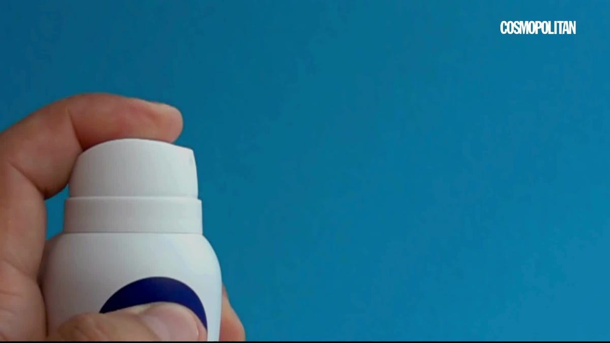 cheerful arab millennial woman with curly long hair in domestic clothes applying deodorant on armpit