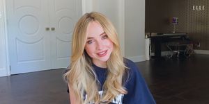 sabrina carpenter sits in her living room wearing a sweater