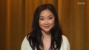 lana condor sits and smiles to the camera against a brown background