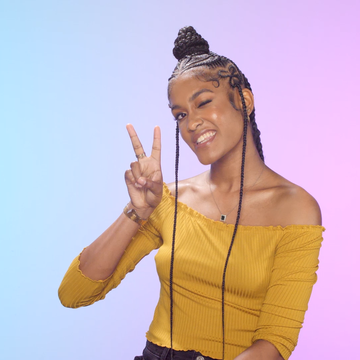 girl with braided hair holds up a peace sign in front of a blue to purple gradient background