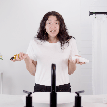 woman stands holding skincare products in front of a sink in a bathroom