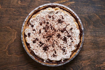 banoffee pie topped with whipped cream and shaved chocolate in a foil pie tin on a dark brown background