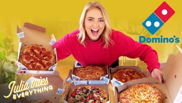 delish host julia smith smiling in front of six open pizza boxes