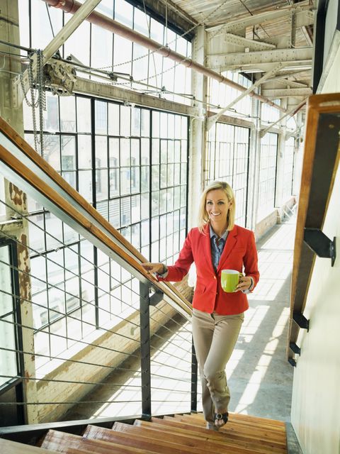 Caucasian businesswoman carrying cup of coffee on warehouse staircase