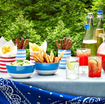 4th of july food picnic table with bowls of dips chips and pretzels and pitcher of lemonade