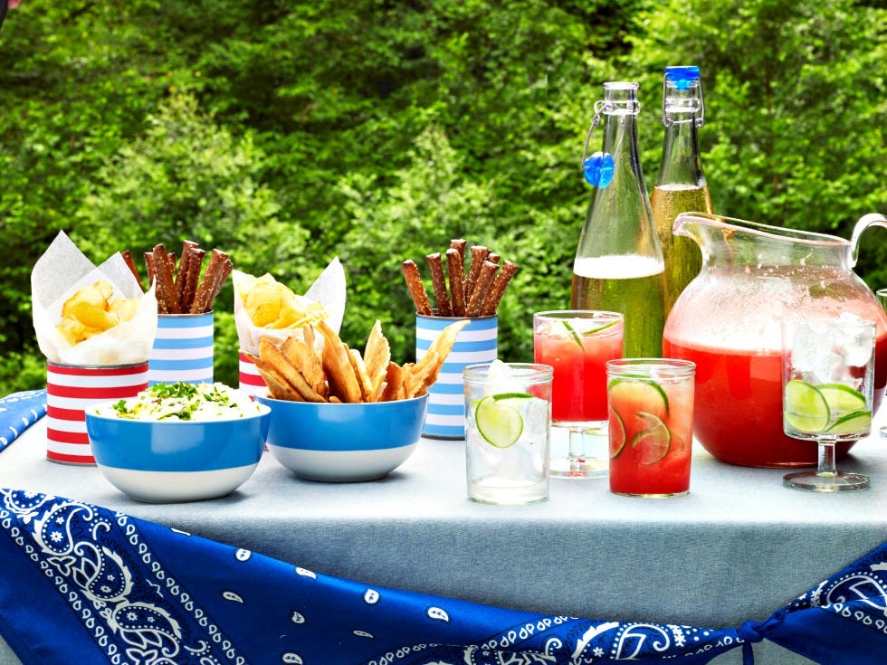 4th of july food picnic table with bowls of dips chips and pretzels and pitcher of lemonade